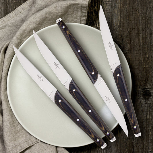Set of four steak knives with wooden handles on a light green plate.