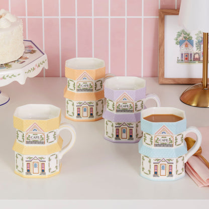 Set of colorful mugs with house designs on a table against a pink tiled wall.