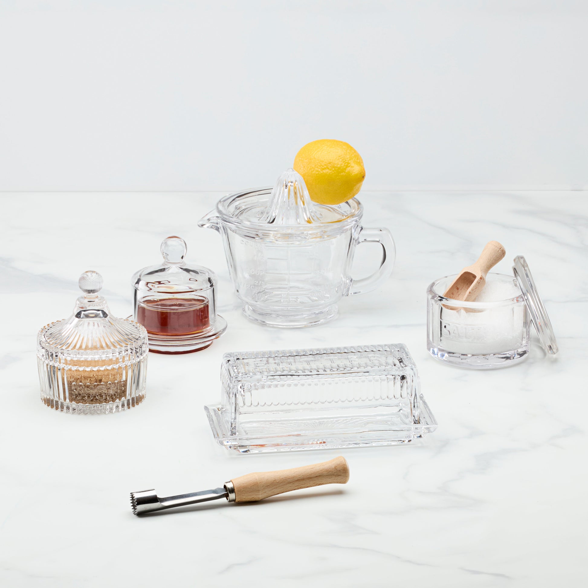 Clear glass kitchenware items including a juicer, bowls, and a citrus reamer on a white background.