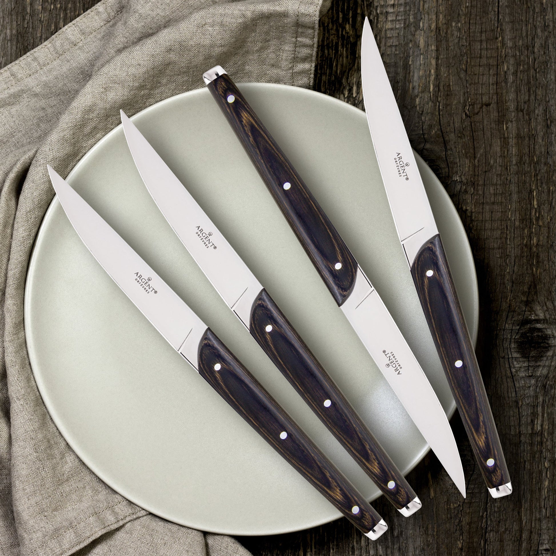 Set of four steak knives with wooden handles on a light green plate.